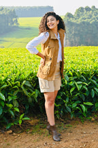 Woman standing in a tea field wearing a brown vest and white shirt.